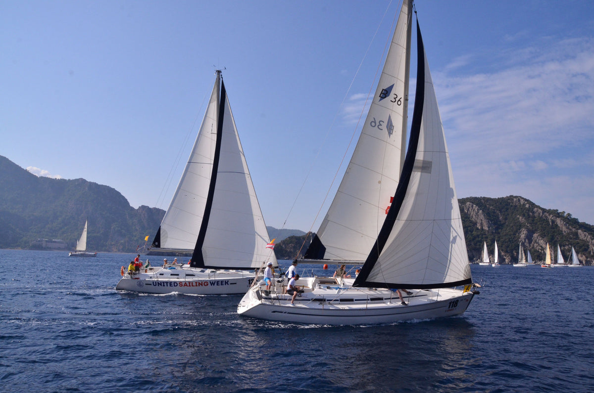 Two white sailboats racing on the blue sea with mountains in the background under a clear blue sky.